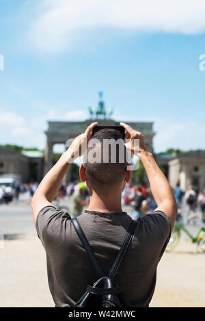 Nahaufnahme eines jungen kaukasischen Mann, von hinten gesehen, ein Bild von der beliebten Brandenburger Tor in Berlin, Deutschland, mit seinem Smartphone Stockfoto