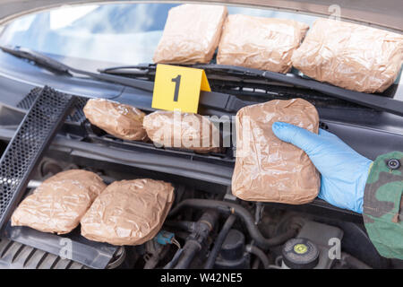 Polizeioffizier holding Droge Paket im Motorraum eines Autos entdeckt Stockfoto