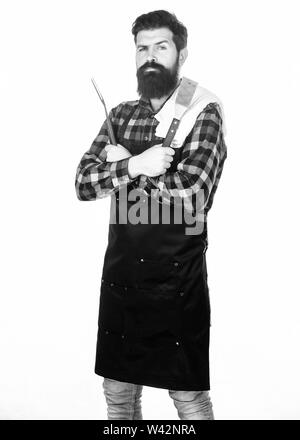 Grill Zubehör. Der bärtige Mann mit Grill Greifer tools. Hipster in Schürze mit Metallgegenstände, Grill. Grill kochen. Kochen Grill. Die Zubereitung von Speisen am Grill mit einem Grill. Stockfoto