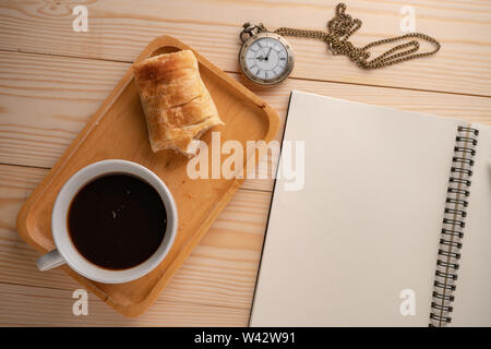 Blick von oben auf die Antique Gold Taschenuhr auf der Seite der Holz- Fach gelegt mit einem weißen Kaffeebecher und die Torte, gebissen worden und Leere noteboo Stockfoto