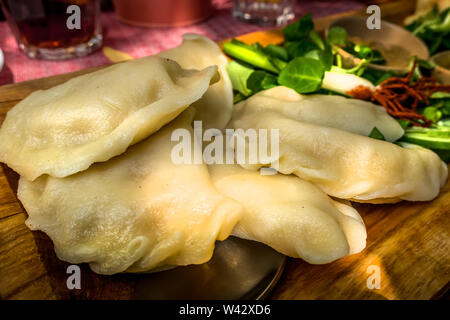 Wareniki, vareniki, polnische Pierogi, pyrohy oder Knödel auf dem Holzbrett mit grünem Salat, traditionelles Essen, Polen Stockfoto