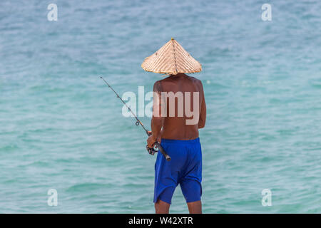 Koh Samui, Thailand - 19 April, 2019: Lokale Mann mit handgefertigten bamboo Hut angeln mit einem Fisch Pole Stockfoto