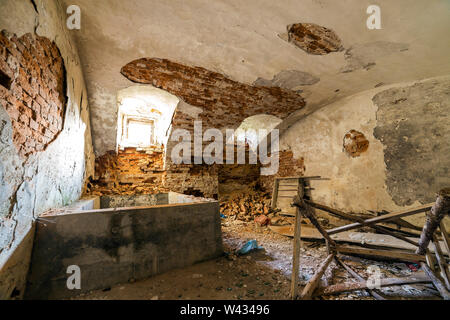 Alte verlassene leere Zimmer im Keller des alten Gebäudes oder Palace mit Gecrackten verputzte Ziegelwände, niedrige gewölbte Decke, kleine Fenster mit Gittern ein Stockfoto