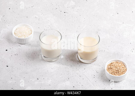 Trinkgläser mit gesunden Reis und Hafermilch, Schüsseln mit Reis Saatgut und Haferflocken auf konkreten Hintergrund. Kostenlose Milch Konzept Lactose. Bild mit Co Stockfoto