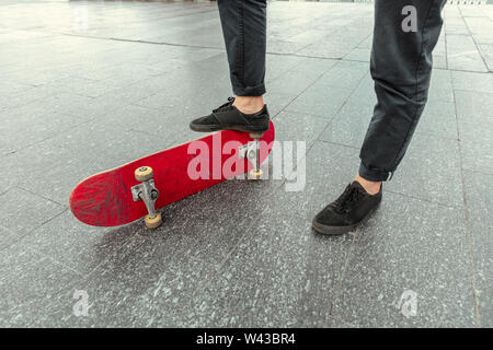 Skateboarder Vorbereitung für das Reiten an der Hauptstraße der Stadt in sonniger Tag. Junger Mann in Sneakers und Kappe mit einem Longboard auf dem Asphalt. Konzept der Freizeitgestaltung, Sport, Extreme, Hobby und Bewegung. Stockfoto