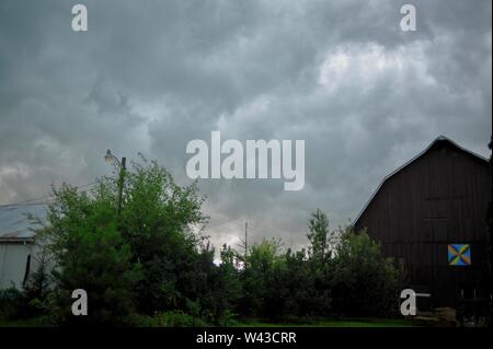 Unwetter und Dunkle, bedrohliche Gewitterwolken Swirl über einen kleinen Hof und Scheune und Nebengebäude und Bäume, Sturm, in Wisconsin, USA. Stockfoto