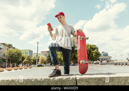 Skateboarder Vorbereitung für das Reiten an der Hauptstraße der Stadt in sonniger Tag. Junger Mann in Sneakers und Kappe mit einem Longboard auf dem Asphalt. Konzept der Freizeitgestaltung, Sport, Extreme, Hobby und Bewegung. Stockfoto