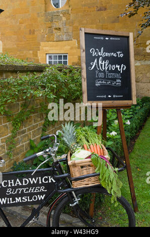 Zeichen auf einer Tafel begrüßen die Besucher der Althorp Essen und Trinken Festival, Northamptonshire, Großbritannien; Vor einer alten Metzgerei Bike mit Gemüse Stockfoto