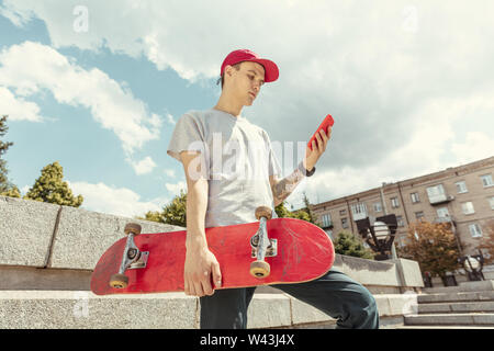 Skateboarder Vorbereitung für das Reiten an der Hauptstraße der Stadt in sonniger Tag. Junger Mann in Sneakers und Kappe mit einem Longboard auf dem Asphalt. Konzept der Freizeitgestaltung, Sport, Extreme, Hobby und Bewegung. Stockfoto