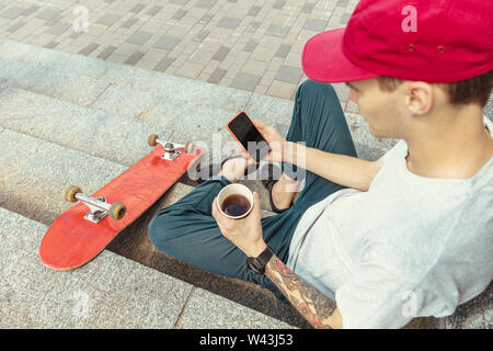 Skateboarder Vorbereitung für das Reiten an der Hauptstraße der Stadt in sonniger Tag. Junger Mann in Sneakers und Kappe mit einem Longboard auf dem Asphalt. Konzept der Freizeitgestaltung, Sport, Extreme, Hobby und Bewegung. Stockfoto