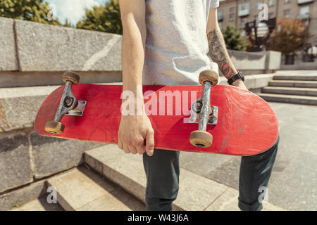 Skateboarder Vorbereitung für das Reiten an der Hauptstraße der Stadt in sonniger Tag. Junger Mann in Sneakers und Kappe mit einem Longboard auf dem Asphalt. Konzept der Freizeitgestaltung, Sport, Extreme, Hobby und Bewegung. Stockfoto