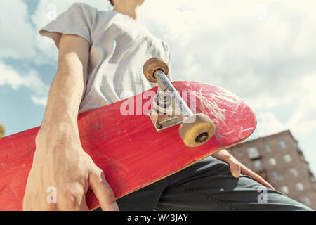 Skateboarder Vorbereitung für das Reiten an der Hauptstraße der Stadt in sonniger Tag. Junger Mann in Sneakers und Kappe mit einem Longboard auf dem Asphalt. Konzept der Freizeitgestaltung, Sport, Extreme, Hobby und Bewegung. Stockfoto