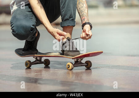 Skateboarder Vorbereitung für das Reiten an der Hauptstraße der Stadt in sonniger Tag. Junger Mann in Sneakers und Kappe mit einem Longboard auf dem Asphalt. Konzept der Freizeitgestaltung, Sport, Extreme, Hobby und Bewegung. Stockfoto