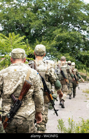 Soldaten der ukrainischen Armee in Uniform mit Chevrons volle Munition und Kalaschnikow Sturmgewehre klicken Sie auf den Ort der Bereitstellung. Stockfoto