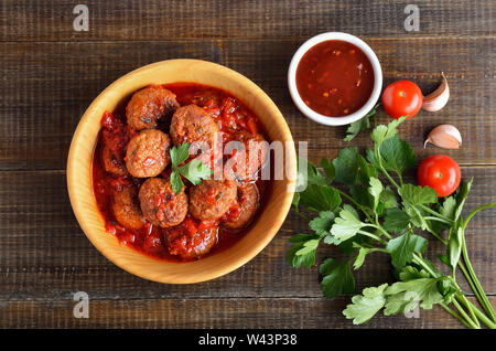 Lecker Frikadellen in Tomatensoße in Holz- platte, Tomatensauce und frischer Petersilie. Ansicht von oben, flach Stockfoto