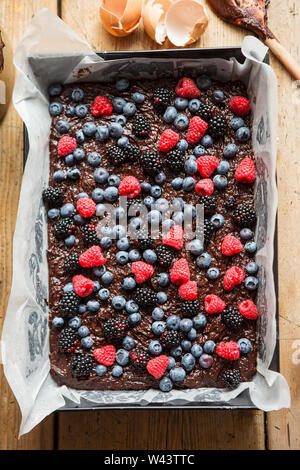 Chocolate Brownie Teig Torte mit Himbeeren, Heidelbeeren und Black in Backblech mit Backpapier auslegen. Backofen bereit Brownies mit Beeren. Stockfoto