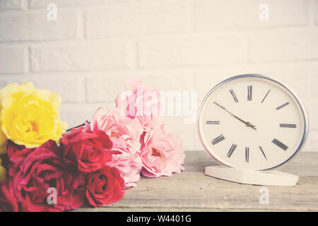 Bunte Rosen und Uhr auf Holztisch auf Mauer Hintergrund Stockfoto