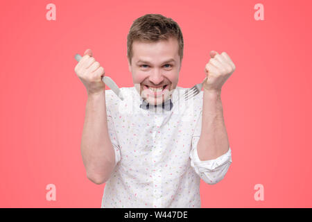 Hungrigen jungen Mann mit Messer und Gabel in der Hand bereit zu essen, Lecken der Lippen. Stockfoto