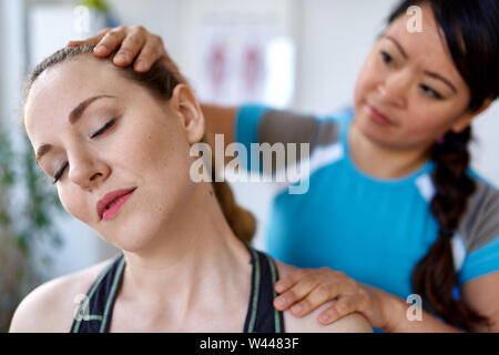 Chinesische Frau Physiotherapie Professional, eine Behandlung zu einer attraktiven Blondine Client in einem hellen Medizinisches Büro Stockfoto