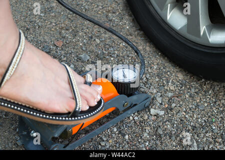 Frau versuchen ein Auto Reifen durch mechanische Luftpumpe aufpumpen. Fuß im Sandal Drücken einer Pumpe betätigen. Nahaufnahme. Sicheres Fahren. Auto Wartung Stockfoto