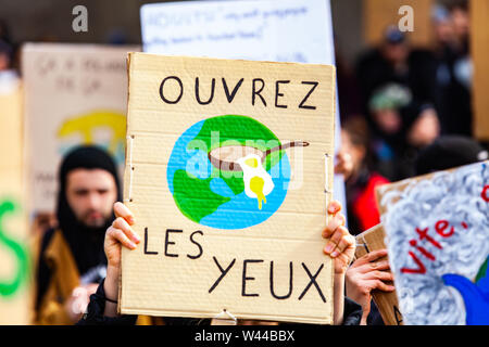 Eine französische Zeichen, sagen ihre Augen öffnen, und der Darstellung der Planet Erde, in den Händen eines Eco gesehen wird - Aktivist während einer Demonstration auf einer belebten Straße Stockfoto