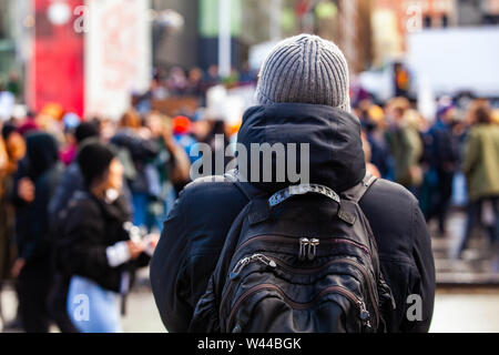 Ein Mann mit einem Rucksack ist von hinten gesehen, als eine große Masse von Umweltschützern unscharf im Hintergrund zu sehen ist. mit Raum für Kopie Stockfoto