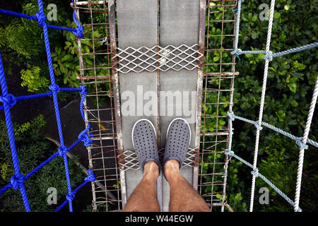 First Person Sicht eines Mannes, der zu seinen Füßen, während auf einer Hängebrücke Stockfoto
