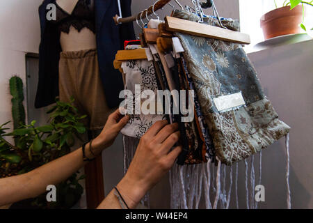 Eine junge Käufer sucht Kleine handgefertigte Taschen in einer Boutique zu speichern. Gemusterte wiederverwendbaren Taschen hängen von einem rustikalen Schiene in einer umweltfreundlichen Freund Stockfoto