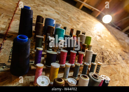 Eine Detailansicht der bunten thread Spools hängend auf einer hölzernen Wand innerhalb einer Art Workshop. Verschiedene Größen hängen an einer Workstation. Stockfoto