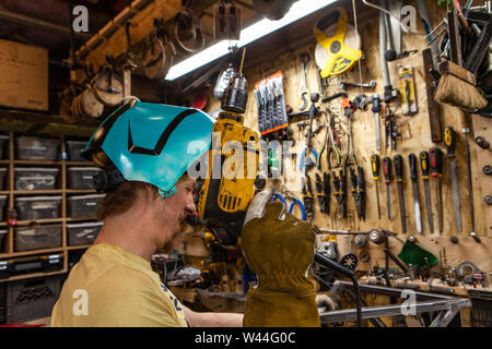 Eine Detailansicht der Schmied Holding eine elektrische Bohrmaschine in seiner Werkstatt. Qualifizierte Handwerker Tragen von Schutzausrüstungen und die Verwendung von Power Tools. Stockfoto