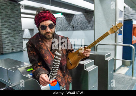 Das Porträt einer Medizin Mann hält sacred Eagle Feather und Holz- Gitarre, wie er lehnt sich gegen die Ticket Erfassung Tore von einem U-Bahnhof, trägt b Stockfoto