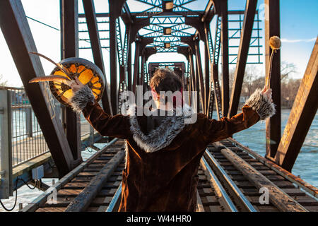 Ein böhmisches Kerl von der Rückseite gesehen wird, die Hände in der Luft mit mystischen Objekte, schließt seine Umgebung einer Eisenbahn Fluss überquert. Stockfoto