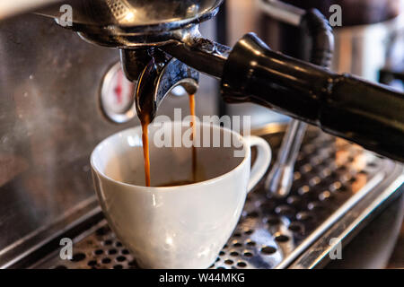 Eine Nahaufnahme auf einem langsamen Tropf Kaffeemaschine Filter in Aktion, erstellen einen Espresso in einem kleinen weißen Schale, gemahlenen Kaffee Bohnen werden mit warmem Wasser gefiltert. Stockfoto