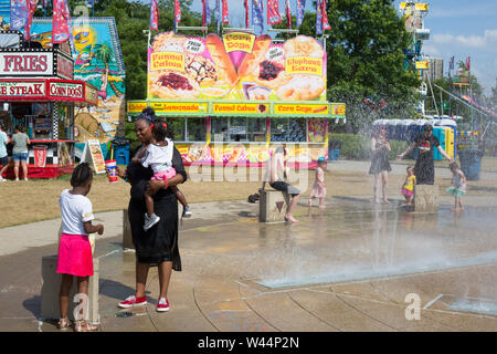 Eine Mutter ermutigt ihre schüchterne Tochter der Splash Pad an den drei Flüssen Festival in der Innenstadt von Fort Wayne, Indiana, USA zu genießen. Stockfoto