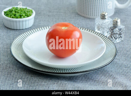 Ganze rote reife Bio Tomaten auf schwarz-weiß gestreiften Platte mit gehacktem grünen Schnittlauch im Querformat. Gesunde Ernährung Konzept. Stockfoto