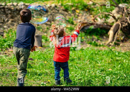 Zwei junge Kinder sind von der Rückseite aus gesehen, zeitversetzte Blasen und Spaß gemeinsam auf einem Campingplatz in der Natur, Bruder und Schwester, mit Kopie Raum auf der rechten Seite. Stockfoto