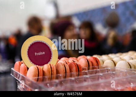 Eine Detailansicht der Strawberry flavoured Macarons (Französisch Makronen) auf einem Regal in einem lokalen Landwirt ist fair, unscharfe Weihnachten Shopper sind im Hintergrund zu sehen. Stockfoto