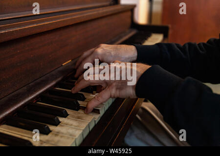 Ein Blick auf die arthritic Hände eines alten Mannes das Spielen einer Melodie auf einem antiken hölzernen Piano. Abgenutzte Tasten werden in den Vordergrund mit Kopie gesehen - Raum. Stockfoto