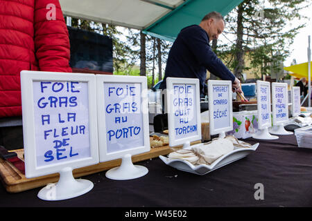 Zeichen, die verschiedene Foie gras Gerichte sind auf den Zähler für ein warmes Essen stand während eines lokalen Messe gesehen, eine glückliche Verkäufer ist verschwommen gesehen, Kochen im Hintergrund Stockfoto