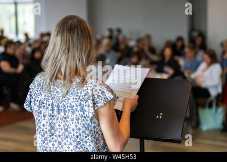 Ein Blick über die Schulter eines Lautsprechers eine Rede auf einem Podium während einer großen Konferenz der Büroangestellten. Blurry Mitarbeiter sind im Hintergrund zu sehen. Stockfoto