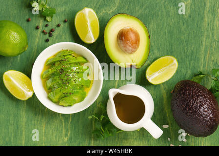 Frische reife Avocado, Kalk, Olivenöl und Gewürzen auf der hellen grünen Holz- Tabelle, Ansicht von oben Zusammensetzung Stockfoto