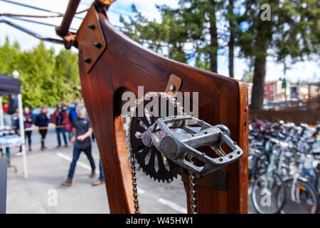 Eine Nahaufnahme auf die Details einer Holz Fahrrad am Ende Metall Ketten & Pedal stand im Vordergrund, abgestellte Fahrräder und blurry Leute im Hintergrund zu sehen sind Stockfoto