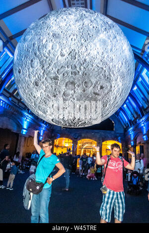 London, Großbritannien, 19. Juli 2019. Die Besucher des Natural History Museum stellen neben einem Modell des Mondes. Der lunar Ausstellung war besonders Bevölkerung