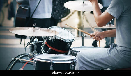 Ein Kerl in grauer Kleidung spielt auf einer Rot und Schwarz mit Holzstäbchen Drum Set, bei einer Präsentation zusammen mit anderen Mitgliedern des musikalischen Straße Stockfoto