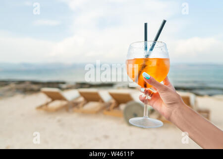 Frau mit köstlichen Classic iced Aperol Spritz Cocktail mit Eiswürfeln an einem heißen tropischen Strand im Sommer Sonnenschein Stockfoto