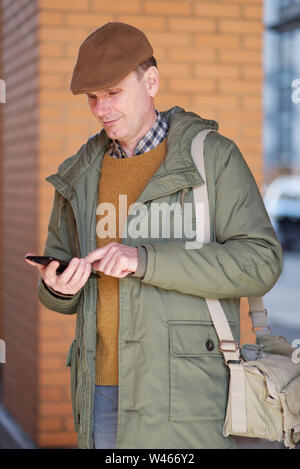 Glückliche Menschen in ungezwungener Winter Kleidung in seinem Smartphone an seiner Wohnung Gebäude suchen Stockfoto