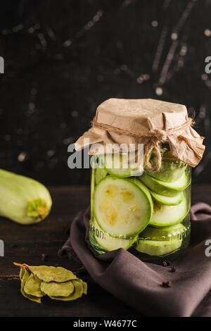 Fermentiert, die Zucchini in einem Glas auf einem dunklen Hintergrund closeup mit Copyspace. Ernte von Gemüse für eine gesunde Ernährung. Stockfoto