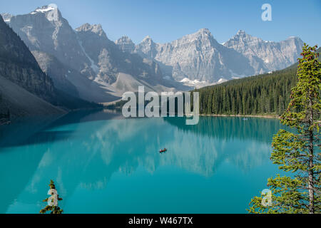 Blick auf das türkisfarbene Wasser des Moraine Lake mit einem Kanu inmitten der Reflexionen der Berge Alberta, Kanada Stockfoto