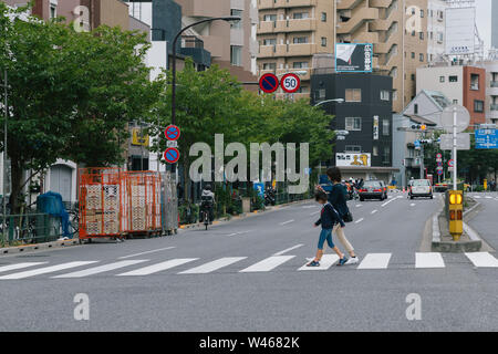 Tokio, Japan - Novemb 15, 2019: Asiatische japanische Mutter mit Smartphone auf der Suche nach Informationen, während die Kreuzung am Zebrastreifen. Stockfoto