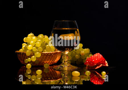 Noch immer leben auf einem dunklen Hintergrund. Wein Likör Gläser, Granatäpfel und Trauben in den Korb. Stockfoto